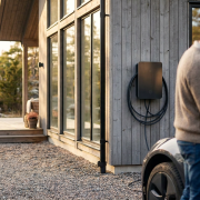 En modern laddbox villa monterad på husfasaden bredvid en parkerad elbil