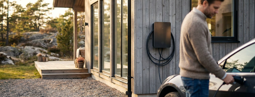 En modern laddbox villa monterad på husfasaden bredvid en parkerad elbil